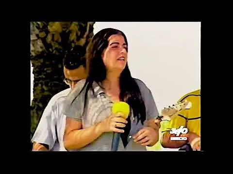 Cantante con un micrófono amarillo durante una actuación televisiva al aire libre
